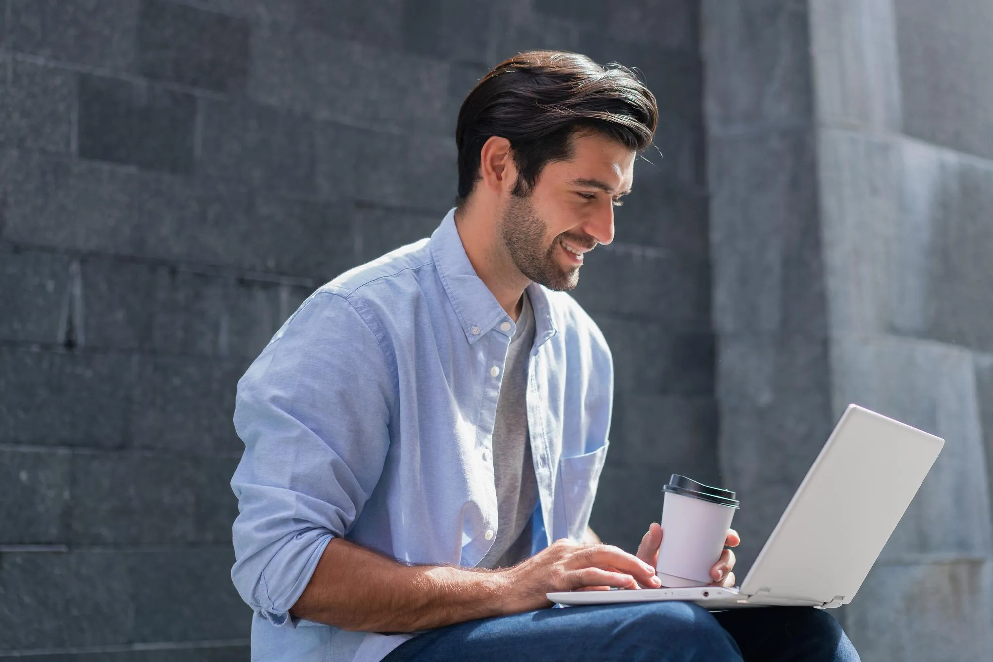 Smiling man sitting outdoors with a coffee, trading on the Deriv MT5 web terminal.