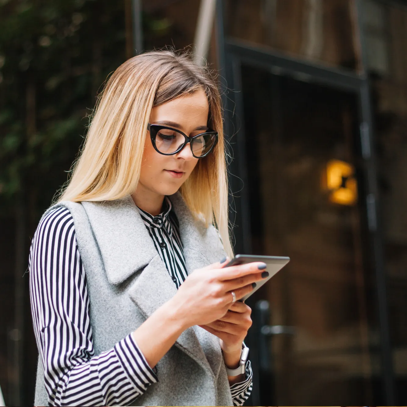 Young woman with glasses analyzing trading markets on a tablet device outdoors.